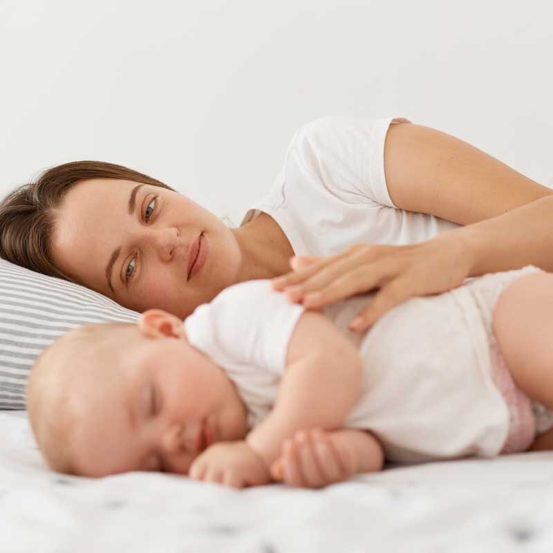 happy-pleased-young-dark-haired-mother-her-baby-lying-together-bed-mommy-hugging-her-charming-daughter-people-wearing-white-clothing-motherhood-childhood